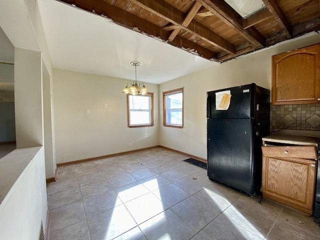 kitchen featuring an inviting chandelier, tasteful backsplash, black fridge, pendant lighting, and light tile patterned floors