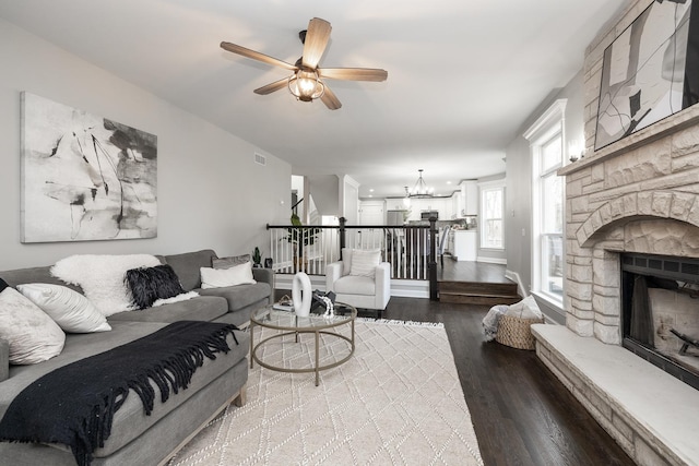 living room with ceiling fan with notable chandelier, wood-type flooring, and a fireplace