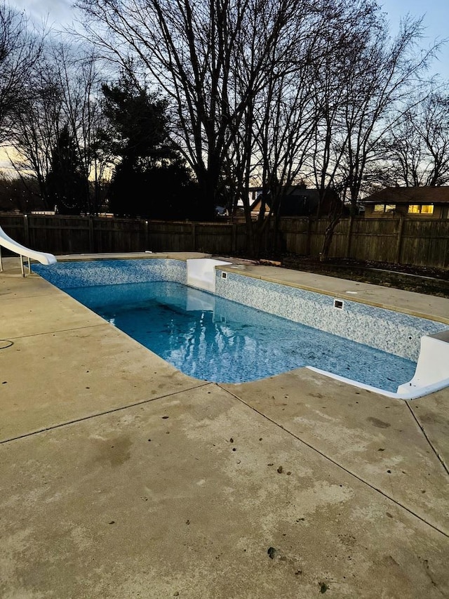 pool at dusk featuring a water slide and a patio