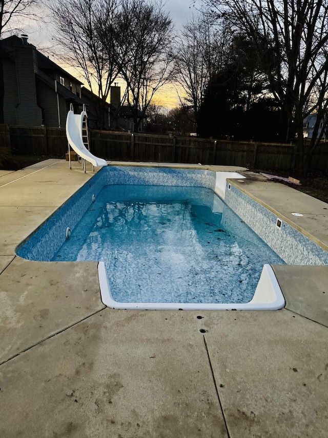 pool at dusk with a patio and a water slide