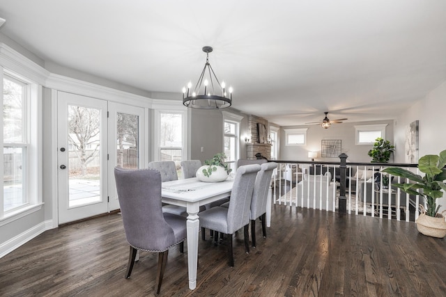 dining space featuring ceiling fan with notable chandelier, a fireplace, and dark wood-type flooring