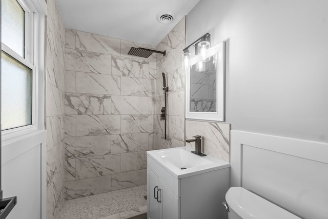 bathroom featuring a tile shower, vanity, and toilet