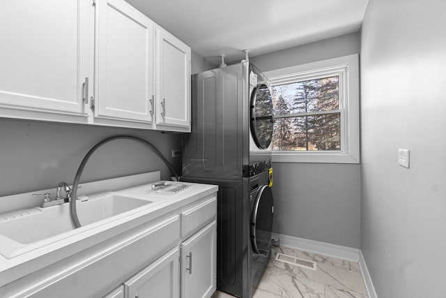 laundry area featuring cabinets, stacked washer and dryer, and sink