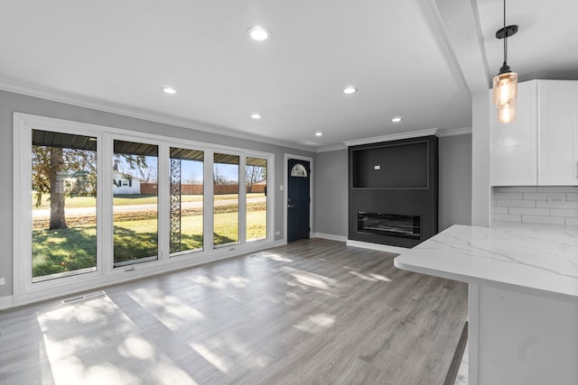 unfurnished living room with a large fireplace, light hardwood / wood-style flooring, a wealth of natural light, and ornamental molding