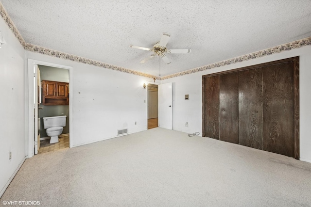 unfurnished bedroom featuring ceiling fan, a textured ceiling, ensuite bathroom, and a closet