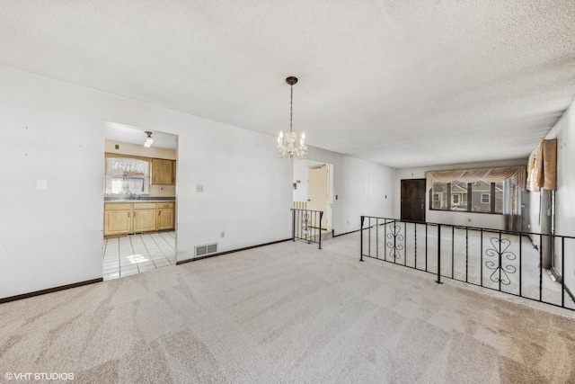 empty room featuring light colored carpet, a textured ceiling, sink, and a notable chandelier