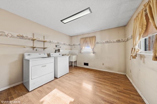 clothes washing area featuring washing machine and dryer, a textured ceiling, light wood-type flooring, and sink