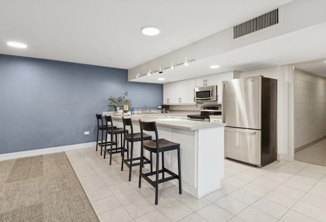 kitchen with stainless steel appliances, kitchen peninsula, a breakfast bar, white cabinetry, and light tile patterned flooring