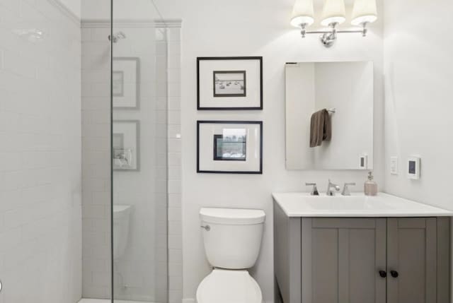 bathroom with toilet, a tile shower, and vanity