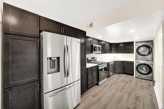 kitchen with sink, stacked washing maching and dryer, stainless steel appliances, light hardwood / wood-style flooring, and decorative backsplash