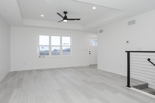 unfurnished living room with a raised ceiling, ceiling fan, and light hardwood / wood-style flooring