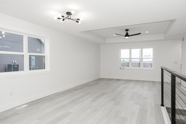 unfurnished living room featuring a raised ceiling, ceiling fan with notable chandelier, and light hardwood / wood-style flooring