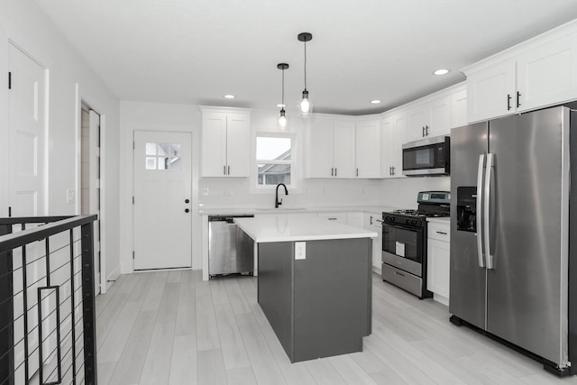 kitchen with white cabinetry, sink, pendant lighting, a kitchen island, and appliances with stainless steel finishes