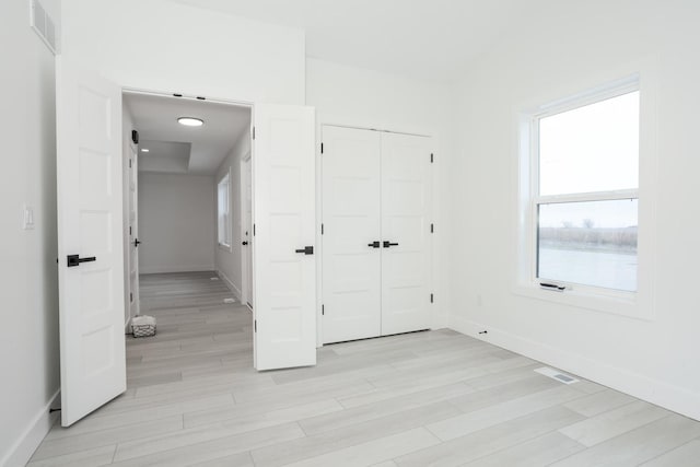 unfurnished bedroom featuring multiple windows, a closet, and light hardwood / wood-style flooring