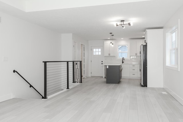 interior space with a kitchen island, decorative light fixtures, light hardwood / wood-style floors, white cabinetry, and stainless steel refrigerator