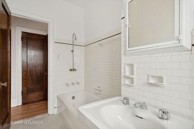 bathroom with tile patterned flooring, tiled shower / bath combo, tile walls, and sink