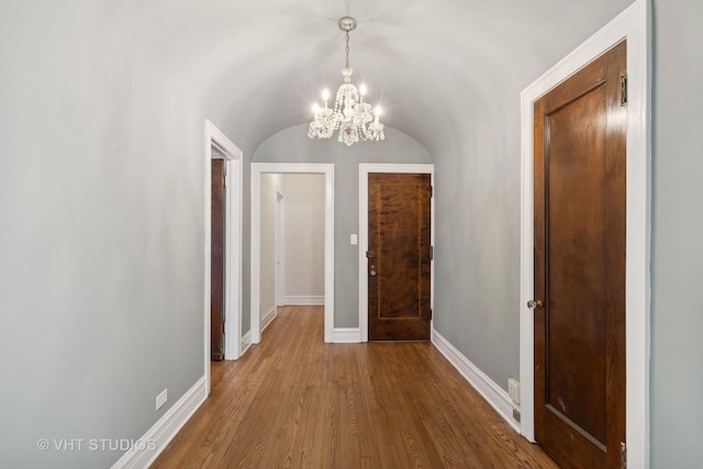 corridor featuring wood-type flooring, lofted ceiling, and an inviting chandelier