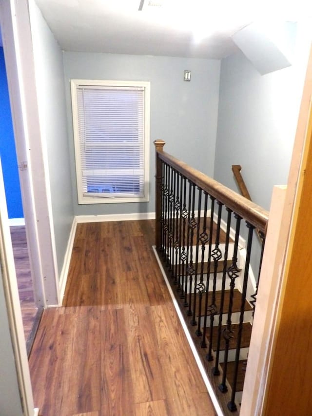 corridor featuring wood finished floors, an upstairs landing, and baseboards