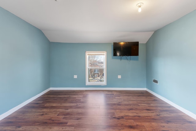 empty room featuring lofted ceiling, baseboards, and wood finished floors