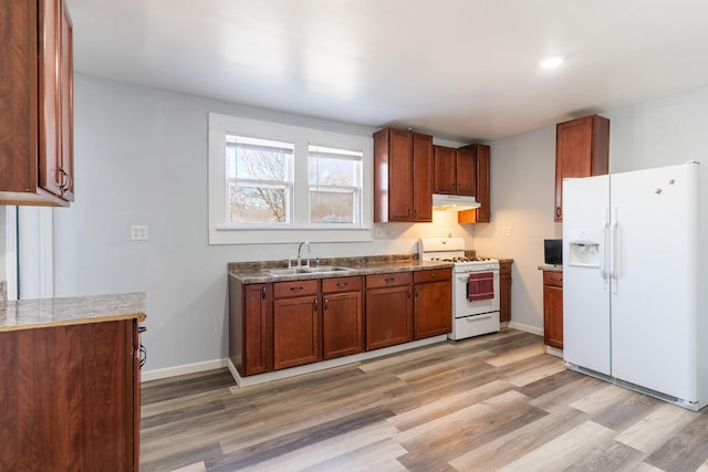 kitchen with white appliances, light wood finished floors, baseboards, under cabinet range hood, and a sink