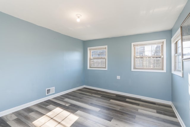 unfurnished room featuring a wealth of natural light, wood finished floors, visible vents, and baseboards