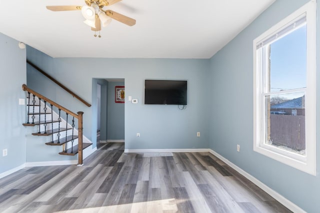 unfurnished living room featuring stairs, wood finished floors, a ceiling fan, and baseboards