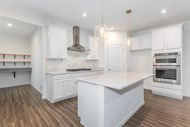 kitchen with wall chimney range hood, appliances with stainless steel finishes, hanging light fixtures, tasteful backsplash, and white cabinets