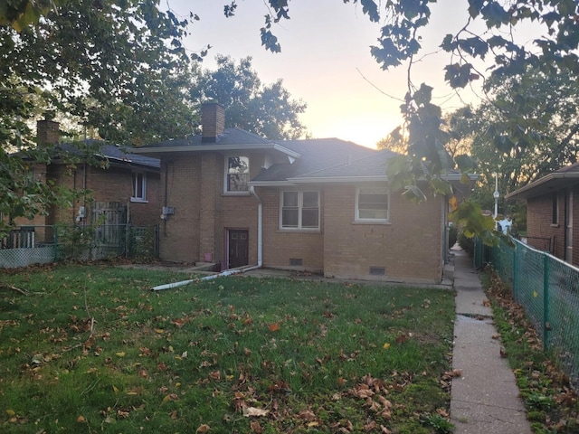 back house at dusk featuring a lawn