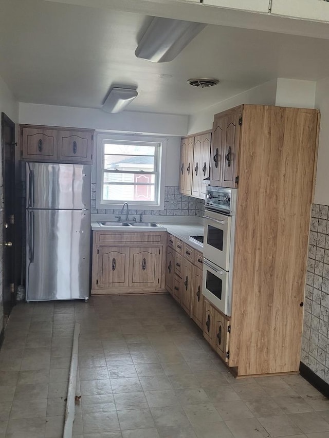 kitchen featuring tasteful backsplash, stainless steel refrigerator, double oven, and sink