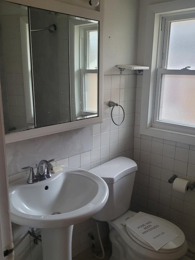 bathroom with toilet, tile walls, and sink