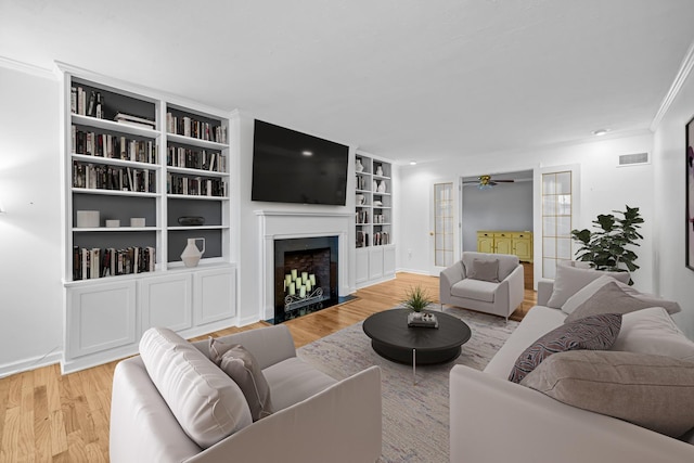 living room featuring french doors, a high end fireplace, ornamental molding, and light wood-type flooring