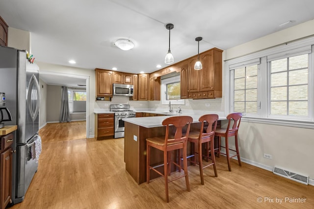 kitchen featuring sink, light hardwood / wood-style flooring, decorative backsplash, appliances with stainless steel finishes, and kitchen peninsula