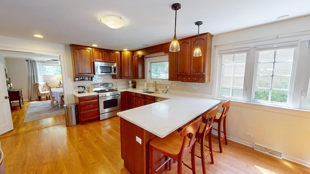 kitchen with backsplash, light wood-type flooring, decorative light fixtures, kitchen peninsula, and stainless steel appliances