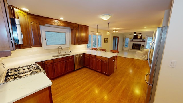 kitchen with sink, kitchen peninsula, pendant lighting, appliances with stainless steel finishes, and light wood-type flooring