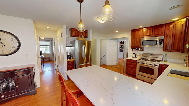 kitchen featuring backsplash, light hardwood / wood-style flooring, appliances with stainless steel finishes, decorative light fixtures, and a kitchen bar