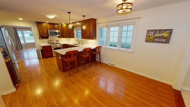 kitchen featuring kitchen peninsula, a breakfast bar, stainless steel appliances, sink, and pendant lighting