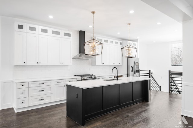 kitchen featuring dark hardwood / wood-style flooring, wall chimney exhaust hood, white cabinets, hanging light fixtures, and an island with sink