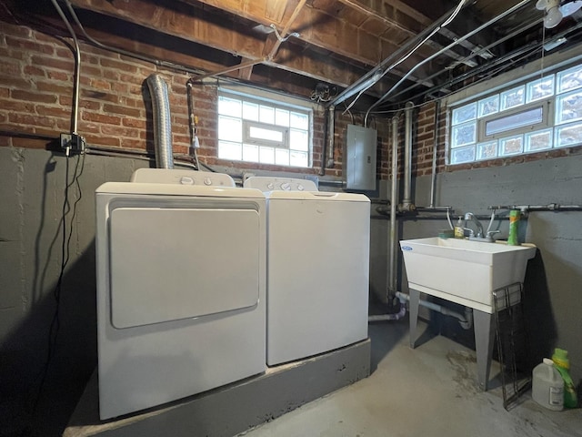 clothes washing area featuring brick wall, washing machine and dryer, sink, and electric panel