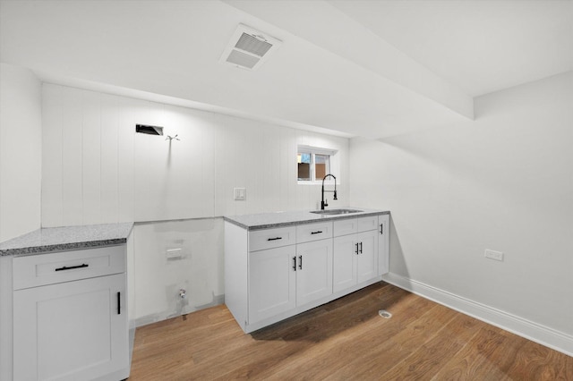 kitchen featuring light stone counters, sink, white cabinets, and light wood-type flooring