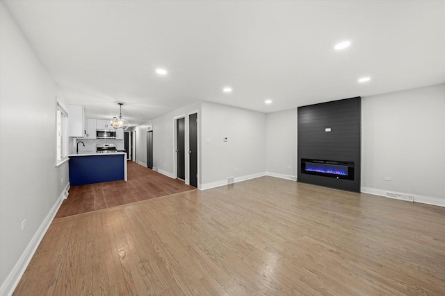 unfurnished living room featuring a chandelier, a large fireplace, light hardwood / wood-style flooring, and sink