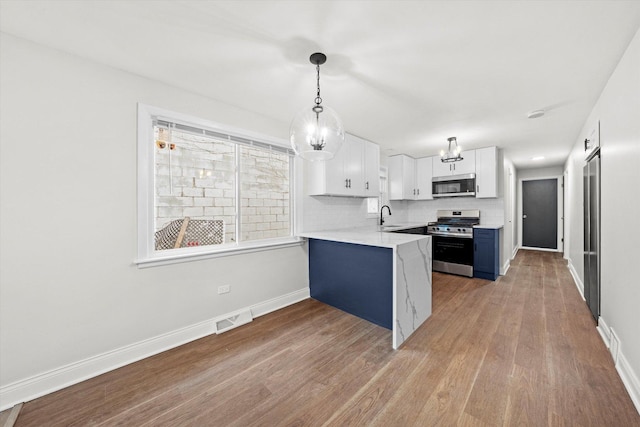 kitchen featuring kitchen peninsula, appliances with stainless steel finishes, blue cabinets, white cabinets, and hardwood / wood-style floors