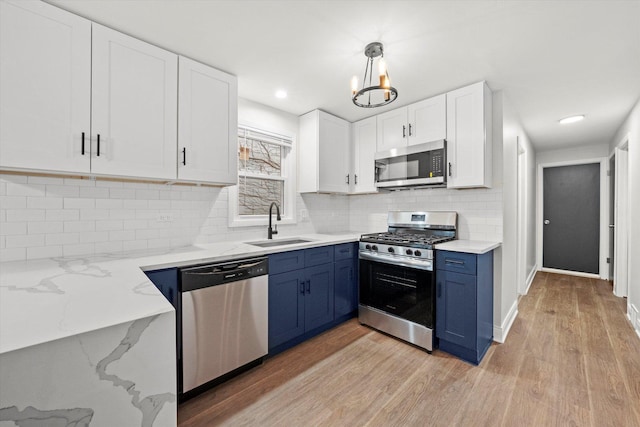 kitchen featuring sink, hanging light fixtures, stainless steel appliances, light hardwood / wood-style flooring, and white cabinets