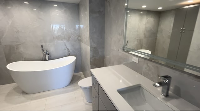 bathroom featuring tile patterned floors, a bathtub, vanity, tile walls, and toilet