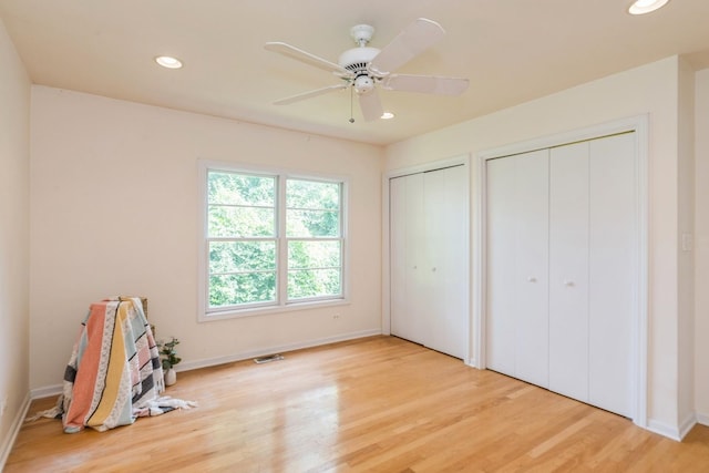 unfurnished bedroom featuring multiple closets, ceiling fan, and light hardwood / wood-style flooring