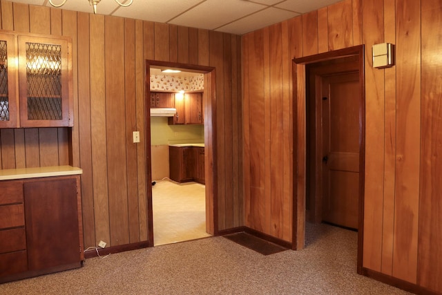 hall featuring dark colored carpet, a paneled ceiling, and wood walls