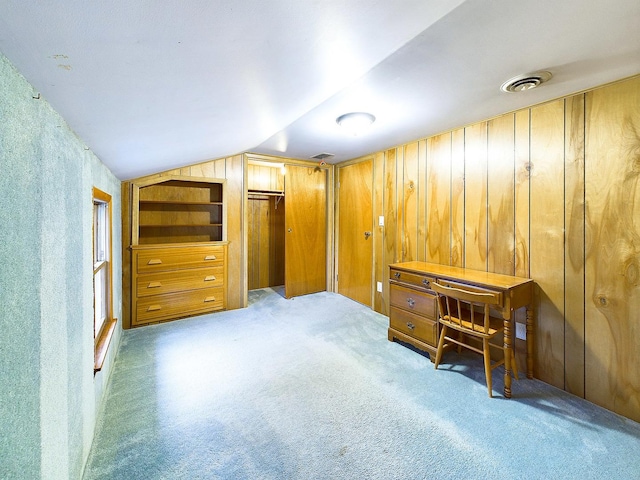 interior space featuring light colored carpet, lofted ceiling, visible vents, and wooden walls