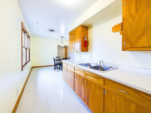 kitchen featuring baseboards, brown cabinets, light countertops, pendant lighting, and a sink