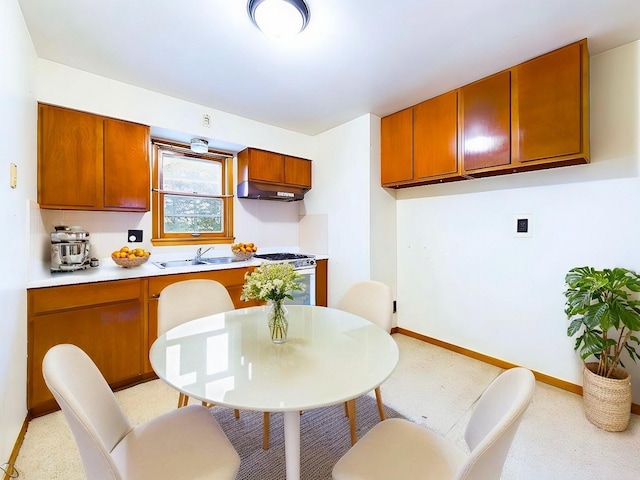 kitchen featuring stainless steel gas range oven, under cabinet range hood, a sink, light countertops, and brown cabinets