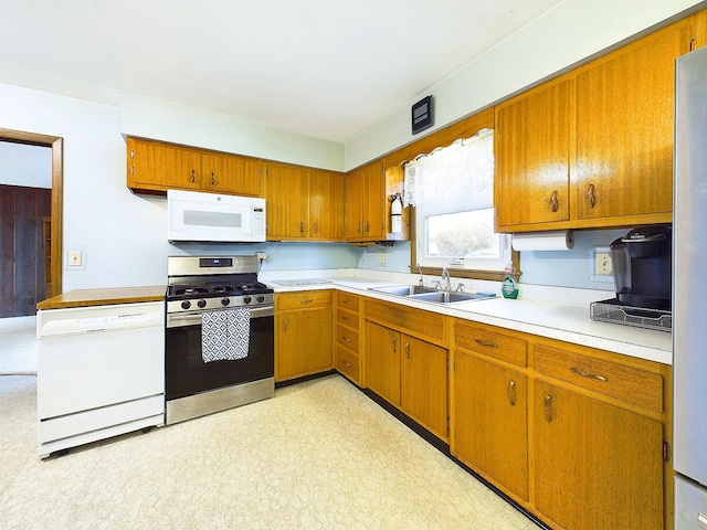 kitchen with light floors, light countertops, brown cabinetry, a sink, and white appliances