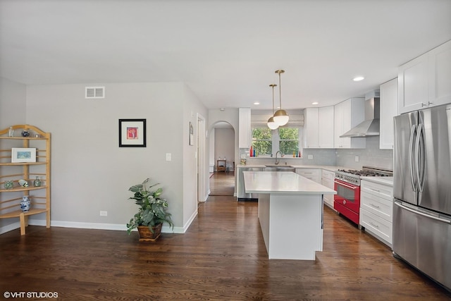 kitchen featuring white cabinets, wall chimney range hood, hanging light fixtures, appliances with stainless steel finishes, and a kitchen island